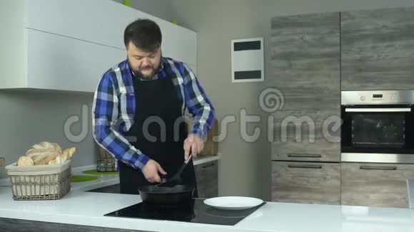 穿着围裙的胖子站在电烤箱附近的厨房里用铲子按下切割片一个厚脸皮的男人视频的预览图