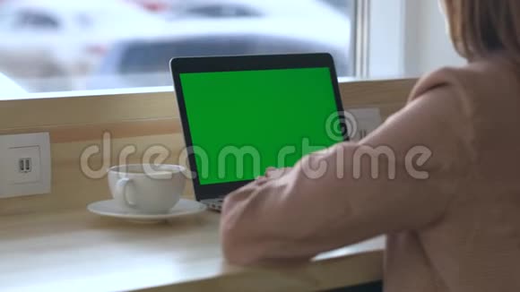 后景女人坐在桌子旁喝咖啡看着笔记本电脑视频的预览图