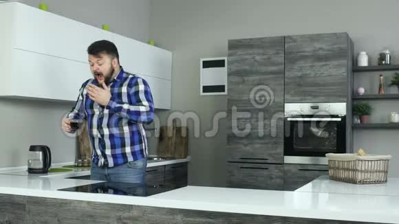 一个困人站在厨房里打哈欠用勺子搅拌咖啡一个昏昏欲睡的家伙在厨房里打哈欠视频的预览图