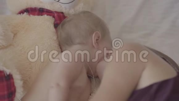 美丽的年轻女子和她的女婴躺在床上亲吻她的脸颊玩具熊就在附近一种概念视频的预览图