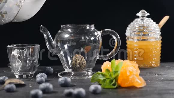 茶叶酿造绿色中国茶花玻璃茶点在木制背景蓝莓玻璃罐加蜂蜜浇注视频的预览图