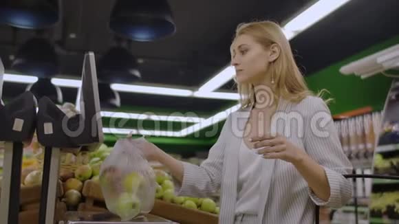 年轻女子称电子秤苹果在水果和蔬菜部的超市购物视频的预览图