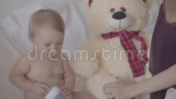 可爱的小女孩坐在床上玩着奶瓶玩具熊就在附近视频的预览图
