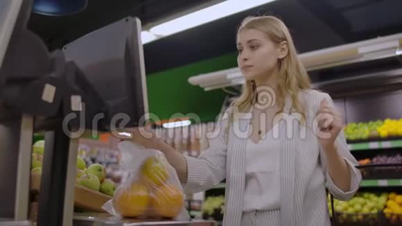 超市里的一个金发女孩用电子秤称着橘子压着摆件摆件上放着篮子视频的预览图