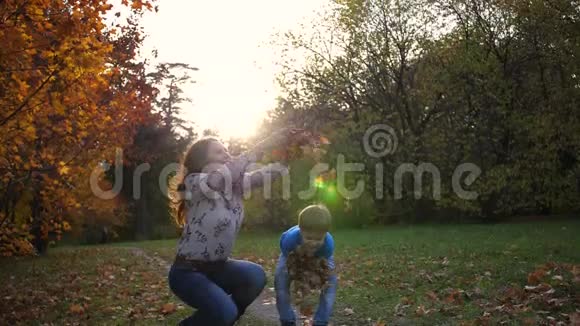秋天公园里的妈妈和孩子扔黄叶微笑着幸福的家庭视频的预览图