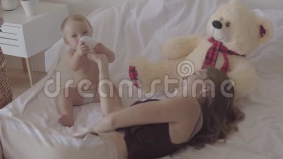 美丽的年轻女人从躺在床上的婴儿瓶里喂她的女婴幸福家庭一个孩子的概念视频的预览图