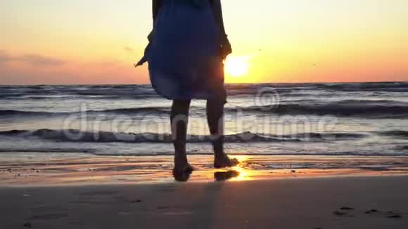 日落时分女孩穿着连衣裙光着脚在潮湿的海边沙滩上散步视频的预览图