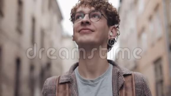 一个戴眼镜戴着检查外套戴着耳机拎着袋子走路的年轻微笑的嬉皮士视频的预览图