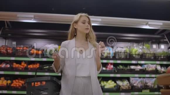 一个漂亮的女人走过超市手里拿着一个篮子看着水果的架子购买新鲜食品视频的预览图