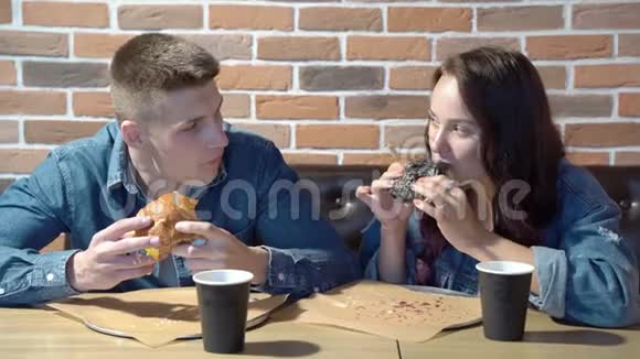 快乐的一对可爱的夫妇在咖啡馆或家里聊天和吃汉堡包视频的预览图