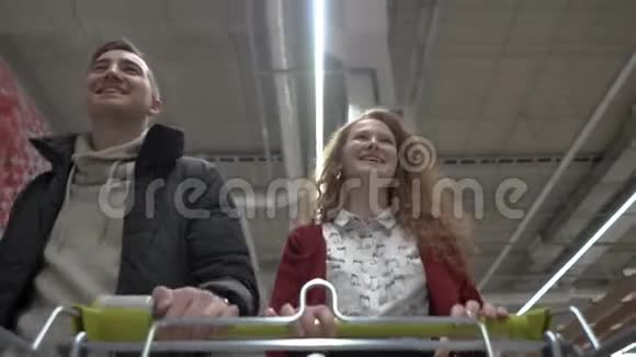 年轻漂亮的女人和男人穿过超市购物车视图视频的预览图