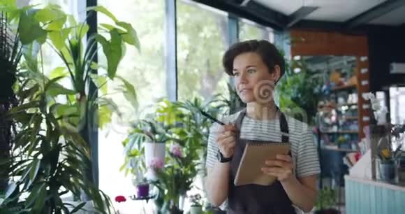 美丽的女士数着植物在花店里的笔记本上写着数据视频的预览图