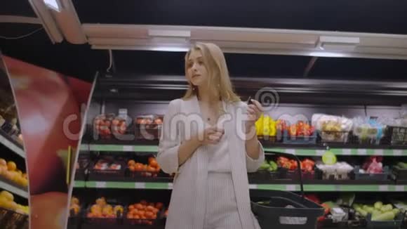 一个漂亮的女人走过超市手里拿着一个篮子看着水果的架子购买新鲜食品视频的预览图
