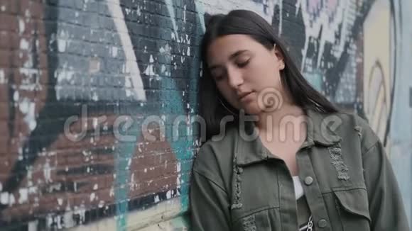 一个年轻悲伤的黑发女孩的肖像棕色的眼睛靠近墙上涂鸦视频的预览图