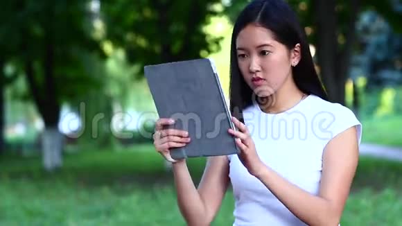 年轻美丽的亚洲人在绿色公园里手挽手谈论平板浪潮视频的预览图