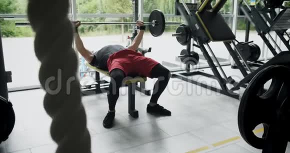 年轻运动员在健身房做板凳压人躺在长凳上用杠铃做运动慢动作视频的预览图