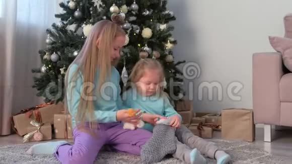 两个孩子的姐妹在家里坐在圣诞树附近玩玩具视频的预览图