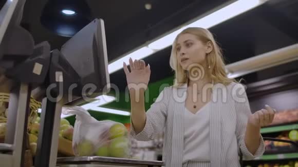 年轻女子称电子秤苹果在水果和蔬菜部的超市购物视频的预览图