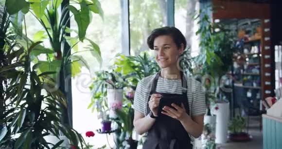 漂亮的女花匠在忙着工作的平板电脑里数着植物的记录视频的预览图