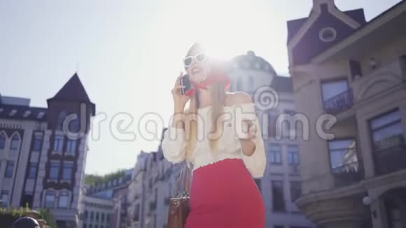 时尚漂亮的年轻女人带着一杯咖啡站在街上晒太阳用手机说话吸引力视频的预览图