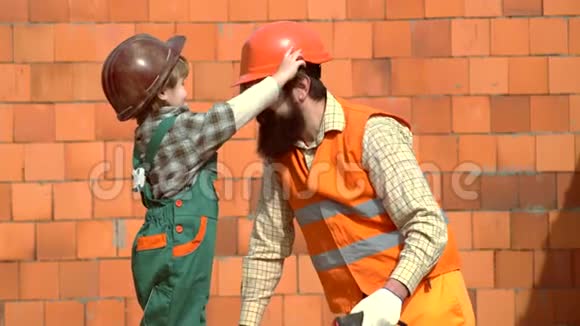 小儿子工人竖起砖墙戴着安全帽的儿子帮助他的父亲父子一起建房子儿子视频的预览图