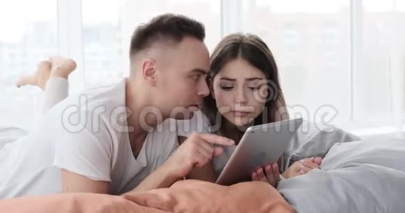 一对夫妇在床上用数码平板电脑感到惊讶视频的预览图