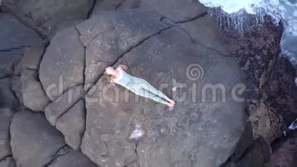 苗条的女人站在海边巨大的灰色石头上做瑜伽姿势视频的预览图