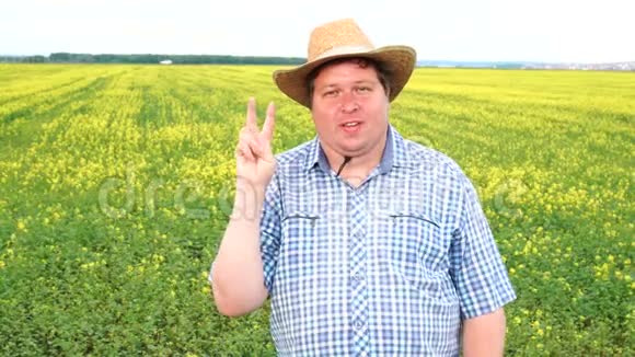 农夫站在田里表现出胜利的迹象在阳光明媚的日子戴牛仔帽视频的预览图
