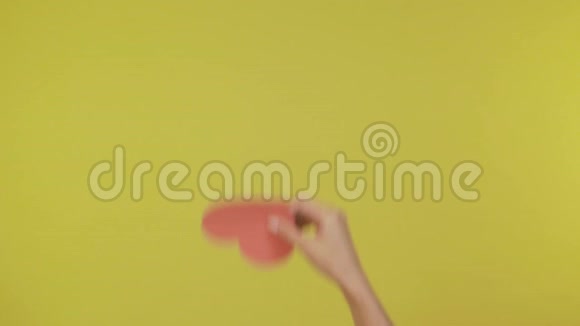 女性的手轻轻地举起和放下纸红色的心在一个孤立的黄色背景4K视频的预览图
