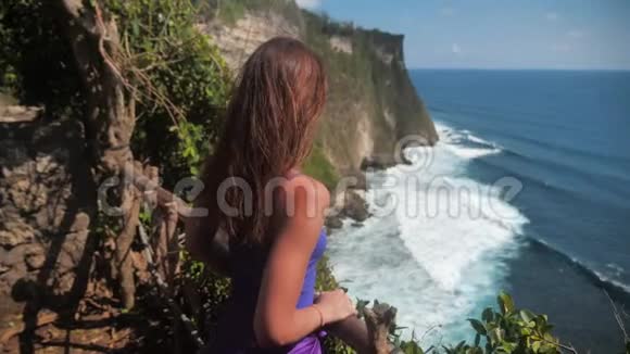 特写肖像一位年轻女子带着棕色头发微笑风吹看着海洋穿绿松石的女孩视频的预览图