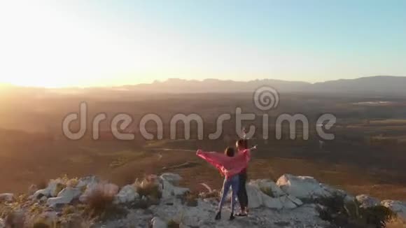 黄昏时分一对年轻夫妇站在山顶上进行公路旅行视频的预览图