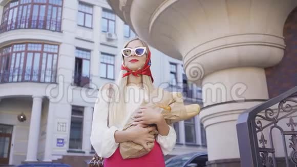站在街上拿着刚出炉的面包和羊角面包的漂亮年轻女人的肖像时尚迷人视频的预览图