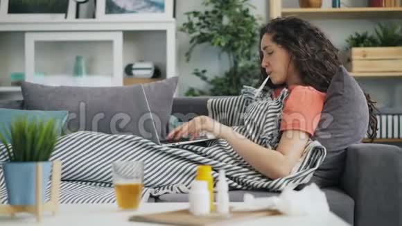 在家里用笔记本电脑咳嗽和流鼻涕的年轻女士视频的预览图