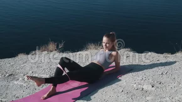 女孩躺在垫子上用橡皮筋做运动训练她的臀部和身体视频的预览图
