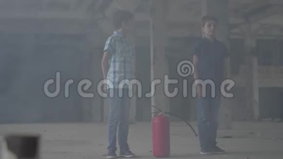 两个小男孩站在黑暗的烟雾弥漫的房间里看着灭火器防火易燃非燃烧概念视频的预览图