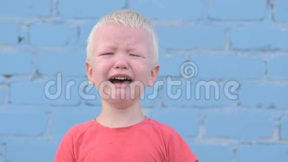 穿着红色T恤的金发小男孩在灰色砖墙上泪流满面视频的预览图