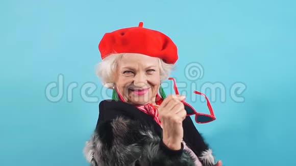 时尚开朗的漂亮奶奶戴着红色的帽子毛皮外套拿着太阳镜摆在相机上视频的预览图