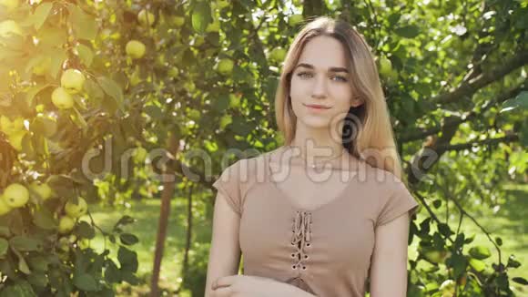 美丽的17岁女孩金发碧眼在苹果树的树枝上摆姿势视频的预览图