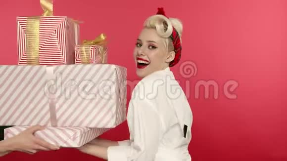 笑着把女孩捏在粉红色背景上拿着礼物盒视频的预览图