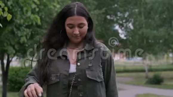 一个长着长发的开朗的黑发女孩在公园里随着音乐跳舞手里拿着一个便携式扬声器视频的预览图