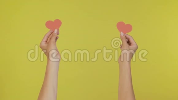 女性的手在一个孤立的黄色背景上用纸心玩亲吻4K视频的预览图