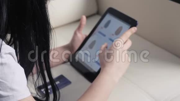 女孩用数字平板电脑制作网上购物概念黑发女人躺在沙发上看着网上商店付钱视频的预览图