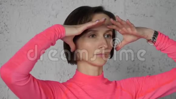 惊讶的女人看得很远当脸瑜伽时双手握在额头上做面部体操的年轻女子视频的预览图