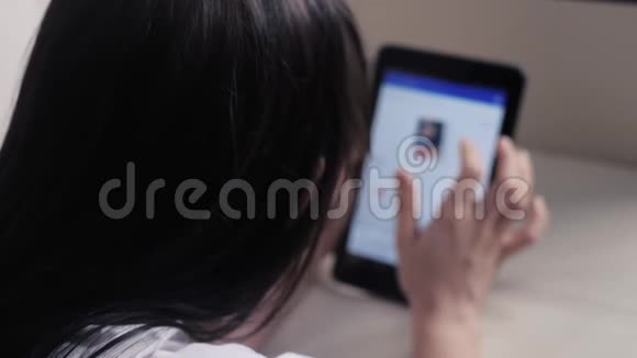 女孩用数字平板电脑制作网上销售购物概念黑发女人躺在沙发上看着网上商店付钱视频的预览图
