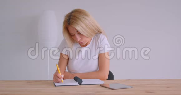 用平板电脑拍摄白种人成年金发女商人的特写肖像并在办公室的室内做笔记视频的预览图