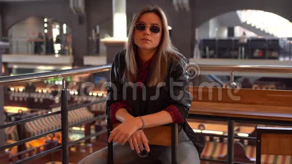 一个漂亮的现代年轻的欧洲女孩穿着黑色皮夹克和牛仔裤留着白发坐在秋天的室内咖啡馆里视频的预览图