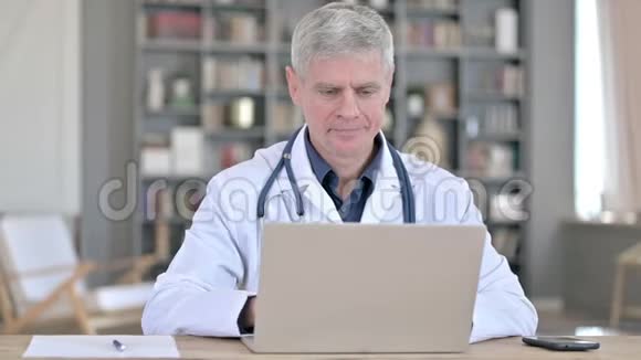 性格开朗的高级医生坐在办公室的时候在笔记本电脑上做视频聊天视频的预览图