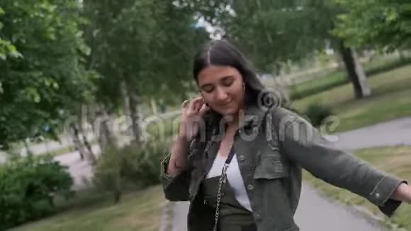 快乐的时髦女孩在公园里随着音乐跳舞手里拿着一个便携式扬声器照相机视频的预览图