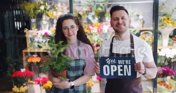 鲜花店男女员工持开放标志及绿植视频的预览图