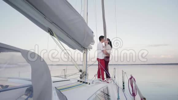 在夜晚的湖面上躺着一艘白色游艇的船头恋爱中的年轻人拥抱着视频的预览图